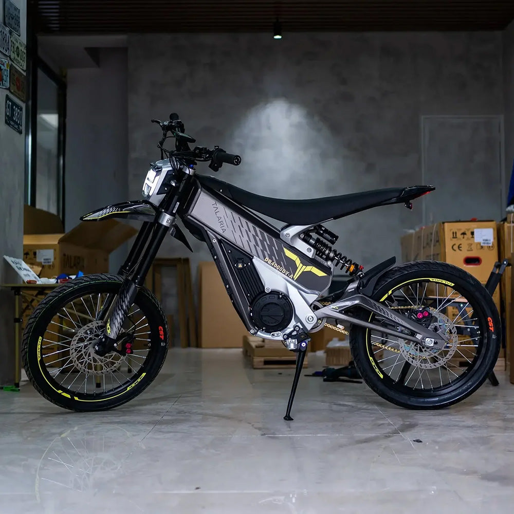 Talaria XXX electric dirt bike side view in a garage setting, highlighting sleek frame, off-road tires, and advanced suspension system