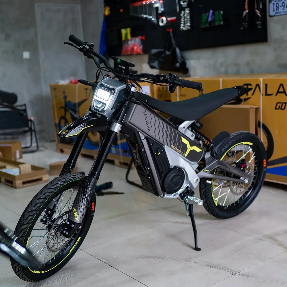 Talaria XXX electric dirt bike in a workshop setting, featuring aggressive front suspension, LED headlight, and high-performance frame design